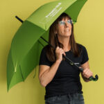 Mitarbeiterin Planungsbüro Projekt HLS mit grünem Regenschirm vor gelbem Hintergrund