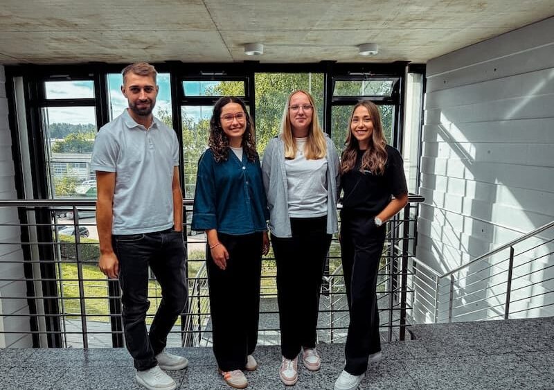 Gruppenfoto bei Projekt-HLS Weiden mit Prokurist Maximilian Brunner (ganz links), den neuen Mitarbeiterinnen Anna (zweite von links, Bauzeichnerin) und Sophie (dritte von links, Auszubildende Technische Systemplanerin), sowie Kollegin Yvonne (ganz rechts) im Eingangsbereich des Unternehmens.