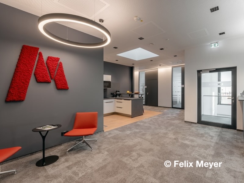 Empfangsbereich im Neubau des Logistikzentrums Markgraf in Kemnath mit rotem Firmenlogo, Sitzlounge und moderner Beleuchtung