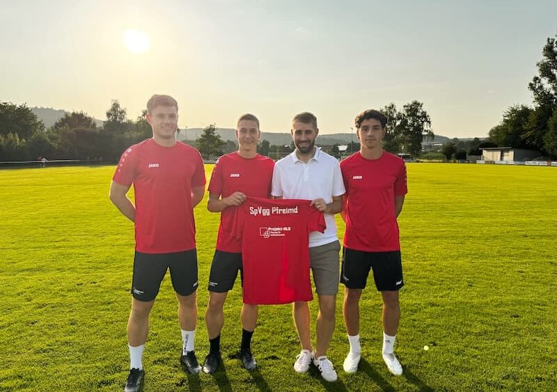 Sponsoring von Projekt-HLS Weiden: Spieler der SpVgg Pfreimd in roten Trikots erhalten neue Trainingskleidung, überreicht von Prokurist Maximilian Brunner auf dem Sportplatz.
